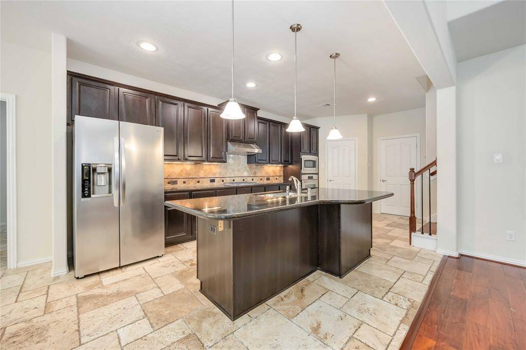 A desirable island kitchen features richly toned cabinets, drop lights over the breakfast bar and island, and under cabinet lighting. In addition, the walk-in pantry rests to the right of the convection oven. The refrigerator is included in the rental.