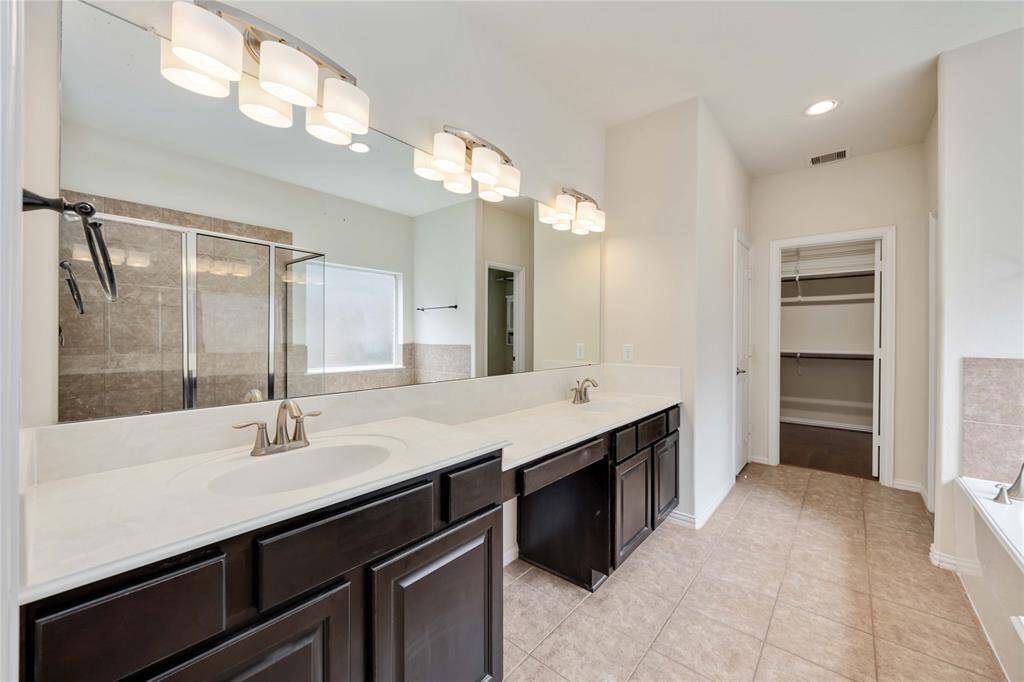 An expansive primary bath means plenty of space for 2 to get ready. A dual sink vanity rests across from a tub and separate shower. The walk-in closet  can be seen in this view.