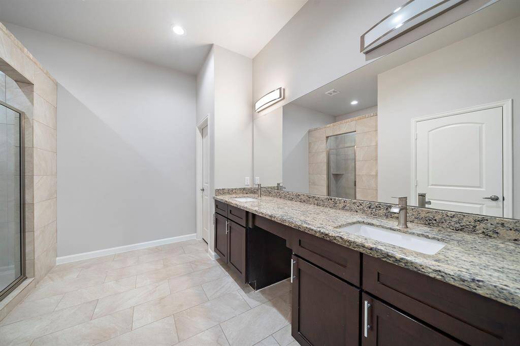 Opulent primary bathroom retreat in a 2017 custom-built home in Panorama Village, perfect for homebuyers seeking luxury and relaxation after a day on the golf course. This expansive space boasts dual double sinks with granite countertops, two separate toilet areas for added privacy, and a spacious stand-up shower with elegant tilework. The whole-home water softener ensures a premium experience, while recessed lighting enhances the bright, airy feel. This bathroom is your perfect putt for a spa-like escape!