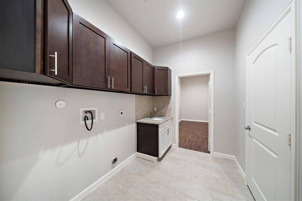 Functional laundry area in a 2017 custom-built home in Panorama Village, designed for homebuyers who value convenience and organization in their golf-inspired lifestyle. This well-appointed space features a door leading directly to the primary walk-in closet, making laundry a breeze, and offers tons of storage with dark cabinetry for all your essentials. A granite-topped sink adds a touch of elegance, while the tiled flooring ensures easy maintenance. This laundry area is your perfect swing for effortless l