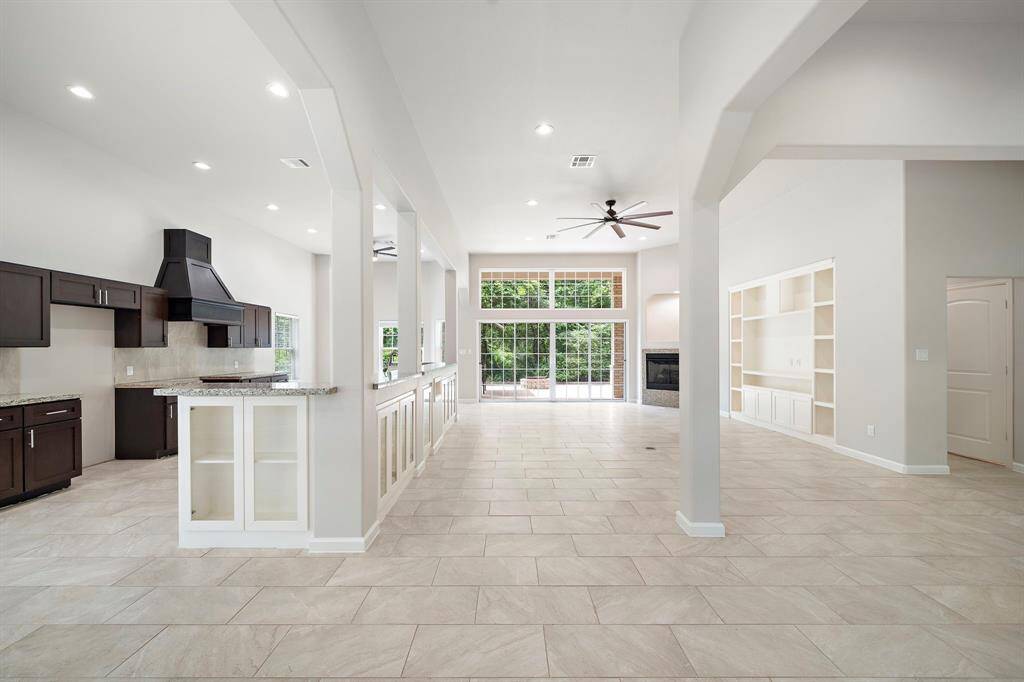 As you enter, the living room unfolds with soaring ceilings, custom built-ins, and large windows that flood the space with natural light, offering serene views of the lush outdoors.