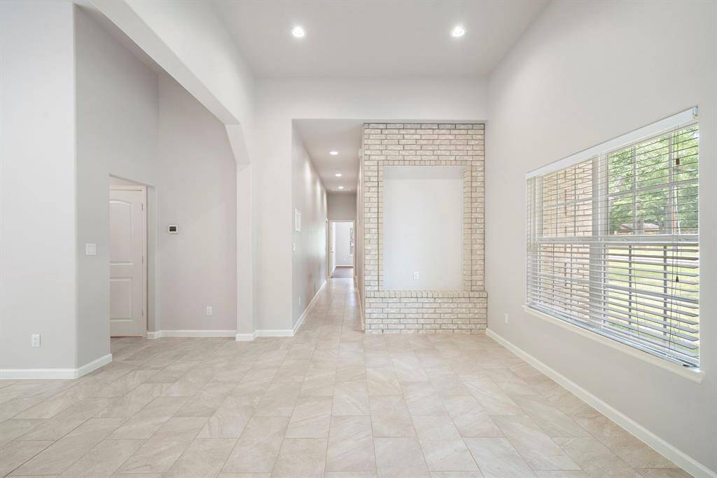 Elegant sitting area awaits at 26 Panorama Drive, Conroe, TX 77304, a custom 2017 home in Panorama Village, perfect for anyone seeking a refined golf course lifestyle. Just off the entrance, this versatile space features a striking brick accent wall, vaulted ceilings, and large windows with plantation shutters, bathing the room in natural light and offering views of the lush surroundings. Ideal for unwinding or greeting guests, this area sets the tone for luxury living. Located on the Panorama Golf Course