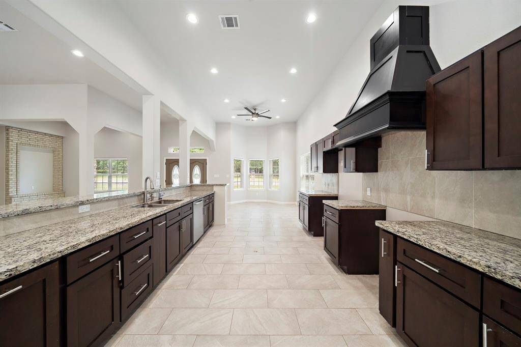 Gourmet kitchen haven in a 2017 custom-built home in Panorama Village, tailored for homebuyers who love to cook and entertain. Overlooking the living area, this chef’s dream features rich dark cabinetry, granite countertops, and a striking range hood, all illuminated by recessed lighting. The open layout ensures seamless interaction with guests, while large windows offer views of the lush surroundings. Positioned on the Panorama Golf Course, enjoy a quick round after breakfast, with Lake Conroe nearby