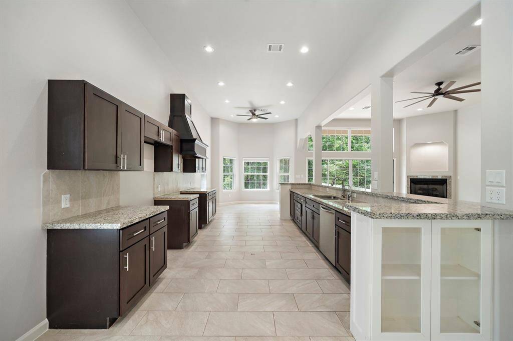 This stunning view into the kitchen is captured from one of two dining areas, showcasing the expansive layout and seamless flow into the living space. The kitchen features an abundance of custom cabinetry, sleek granite countertops, and a generous island—perfect for entertaining or casual meals. Flooded with natural light and surrounded by picture windows, this space is both functional and inviting.