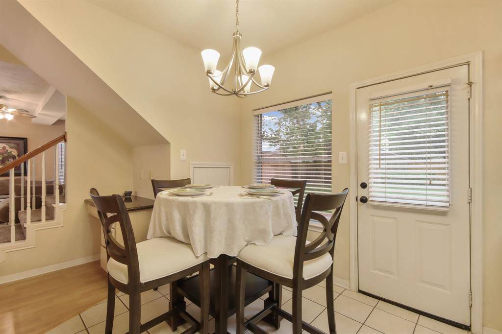 This cozy dining area features  a chandelier, and natural light from large windows. It has direct access to a small patio through a door with blinds, and it’s conveniently located next to a staircase leading to the main living area.