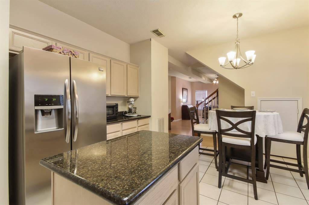 This photo showcases a modern kitchen that leads to a cozy breakfast area with a stylish chandelier and a view of the living space and staircase, creating an open and inviting atmosphere.