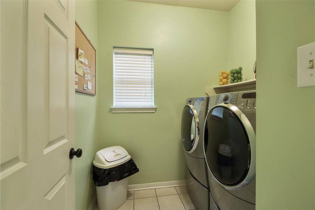 This photo shows a compact laundry room with a modern washer and dryer set, light green walls, a small window with blinds. Located straight through the kitchen.