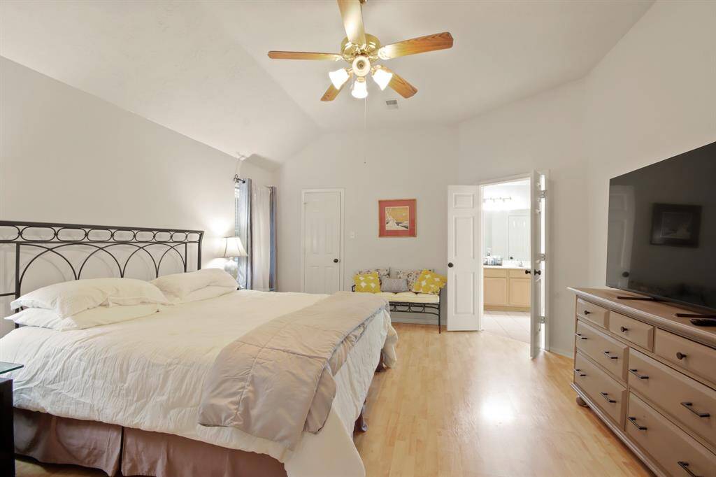 Spacious bedroom with a high ceiling and wood flooring, featuring a ceiling fan, and ample natural light. large enough for  a cozy seating area and access to an en-suite bathroom.