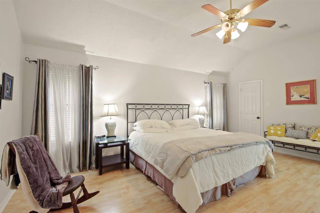 Spacious bedroom with vaulted ceiling, featuring a  ceiling fan, and ample natural light from two windows. Large enough for cozy seating/relaxing area.