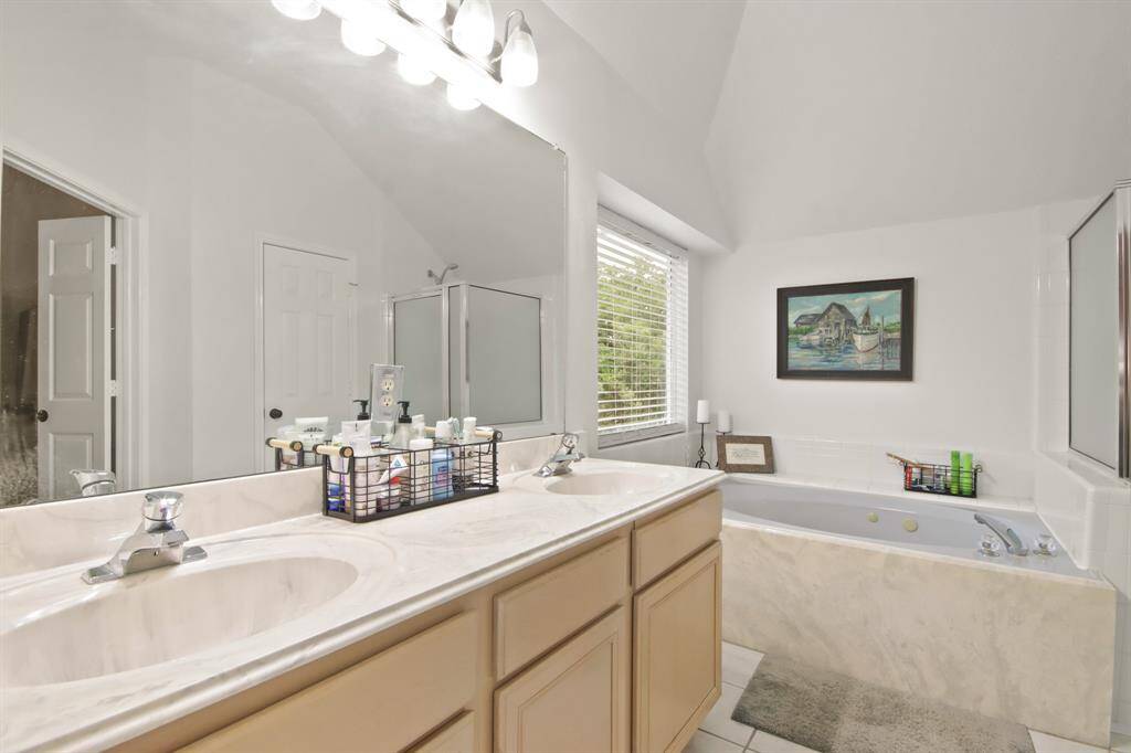 Primary bathroom features a double sink vanity with ample counter space, a large mirror, a spacious bathtub with jets, and a separate shower. Natural light streams through a window, enhancing the bright, airy feel.