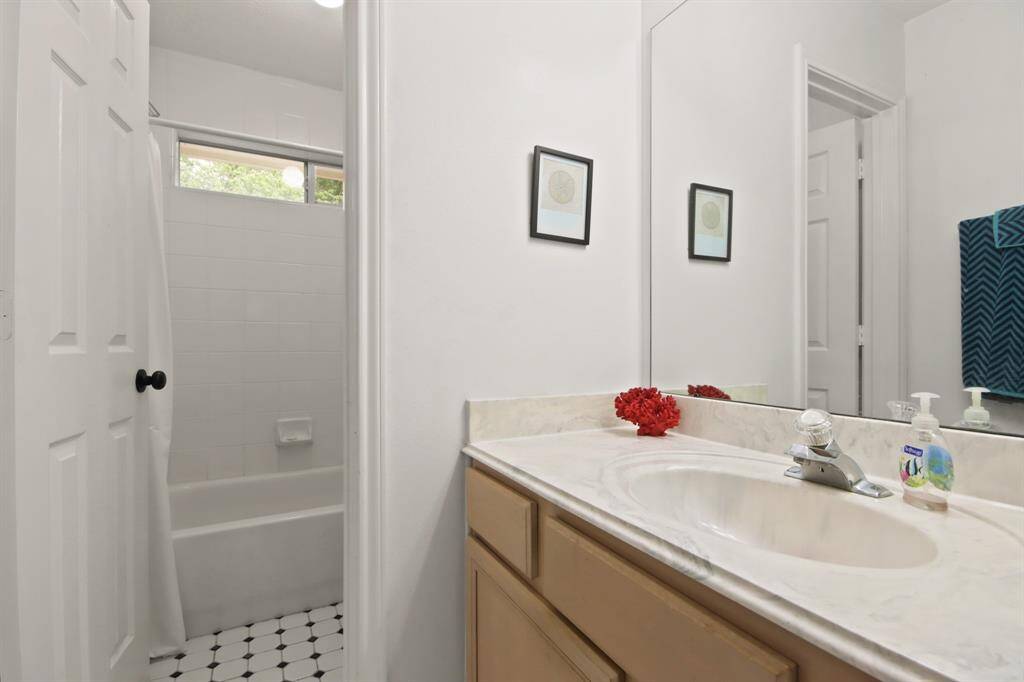 Second bathroom features a clean, bright layout with a large mirror above a single-sink vanity. It has a bathtub with white tiles and a small window for natural light.