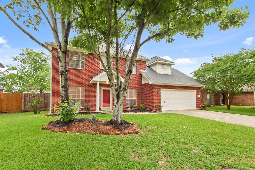 This charming two-story brick home features a welcoming front porch with two pillars, a two-car garage, and a well-maintained lawn with mature trees.