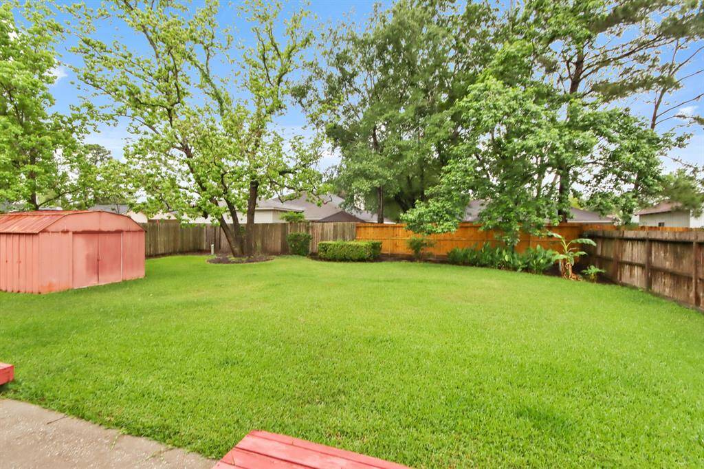 This photo showcases a spacious backyard with lush green grass, mature trees, and a red storage shed, all enclosed by a wooden fence. Ideal for relaxation and outdoor activities.