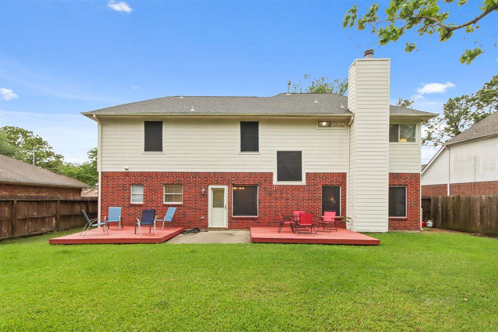 This photo showcases the rear exterior of the two-story home with a combination of brick and siding. It features two wooden decks/patios, a spacious lawn, and a fenced backyard, ideal for outdoor activities, entertaining, or just relaxing.