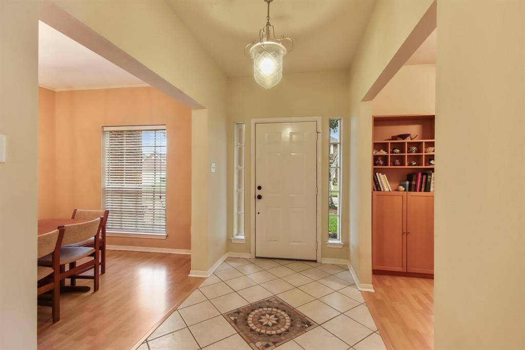 This welcoming entrance features a bright foyer with a tiled floor and a decorative medallion. The adjacent rooms have warm wood flooring, with a dining area on the left and a cozy office area to the right in the picture.