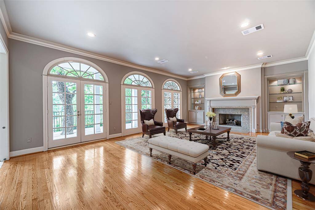 Elegant family room as wood floors, large floor to ceiling windows with doors leading onto the large patio area. The living room has custom details throughout with built in cabinets and glass shelving, wood burning fireplace with tile surround and detailed mantle. *Virtually staged picture*