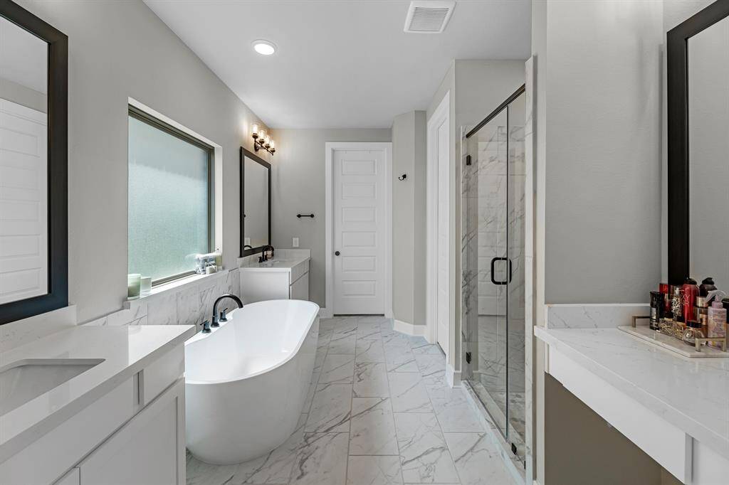 Luxurious primary bathroom with dual sinks, separate vanity area, standing soaking tub, and walk-in shower.
