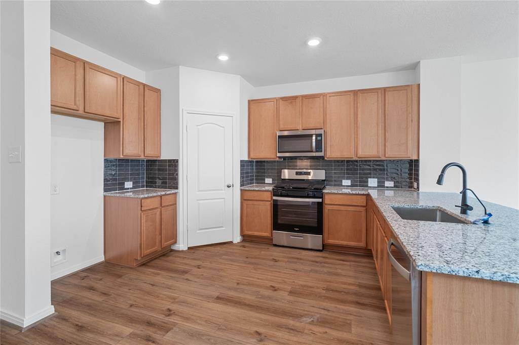 This spacious kitchen features high ceilings, stained wood cabinets, granite countertops, SS appliances, modern tile backsplash, recessed lighting, space for breakfast bar, and a pantry all overlooking your huge family room.