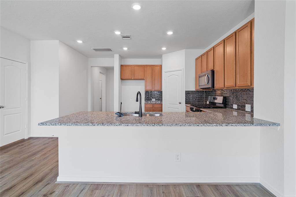 This spacious kitchen features high ceilings, stained wood cabinets, granite countertops, SS appliances, modern tile backsplash, recessed lighting, space for breakfast bar, and a pantry all overlooking your huge family room.