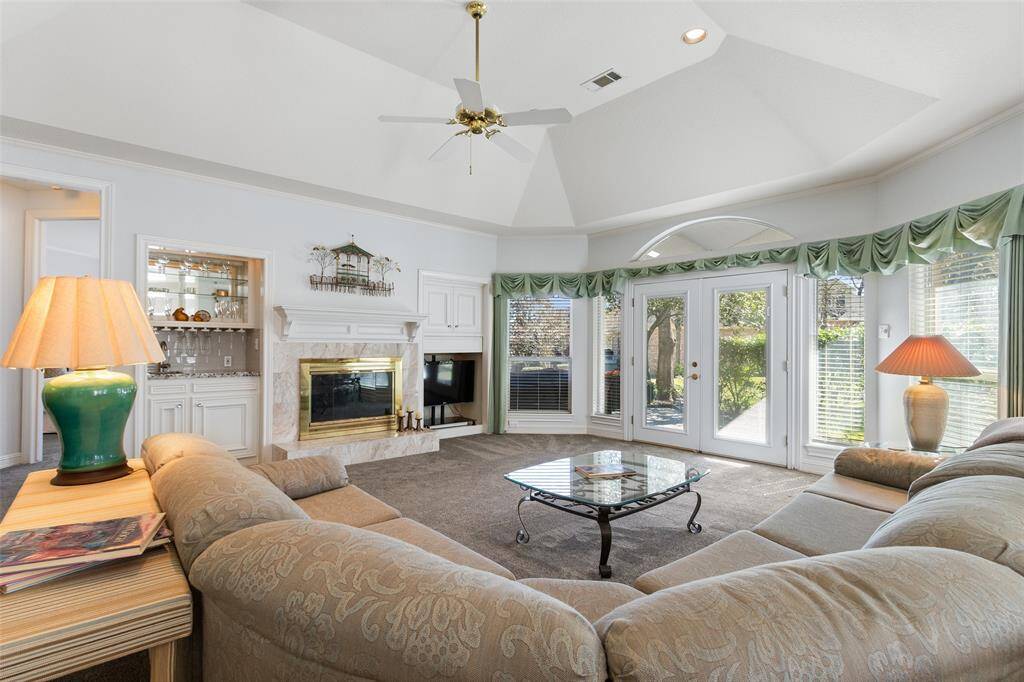 Spacious living area boasts a cozy fireplace flanked by custom cabinets, flowing seamlessly into a sleek wet bar. Expansive windows overlook the covered patio. Host family and friends for holidays in this large space, suitable for multiple seating arrangements.
