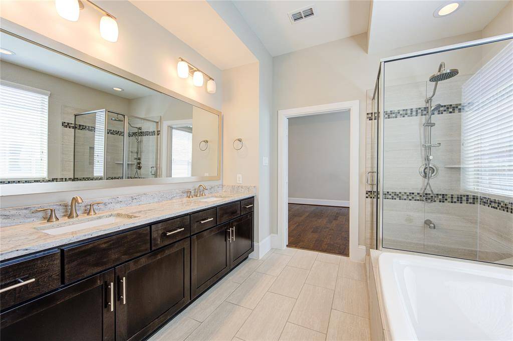 The large primary bath is a work of art with the upgraded cabinet hardware, granite vanity, and mosaic tile inlay in the tub and shower surround.