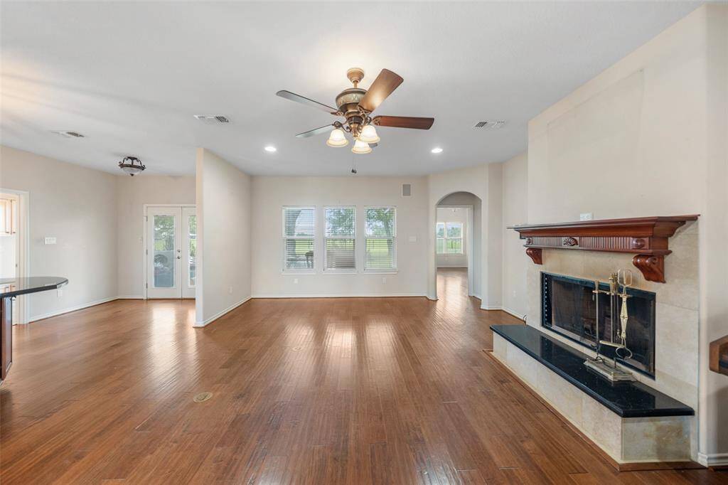 The expansive living area features hardwood floors, a cozy fireplace with a detailed mantel, and direct access to the backyard through French doors.
