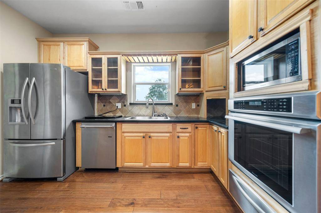 The kitchen pairs stainless steel appliances with warm wood cabinetry and granite countertops, all anchored by a window overlooking the backyard.