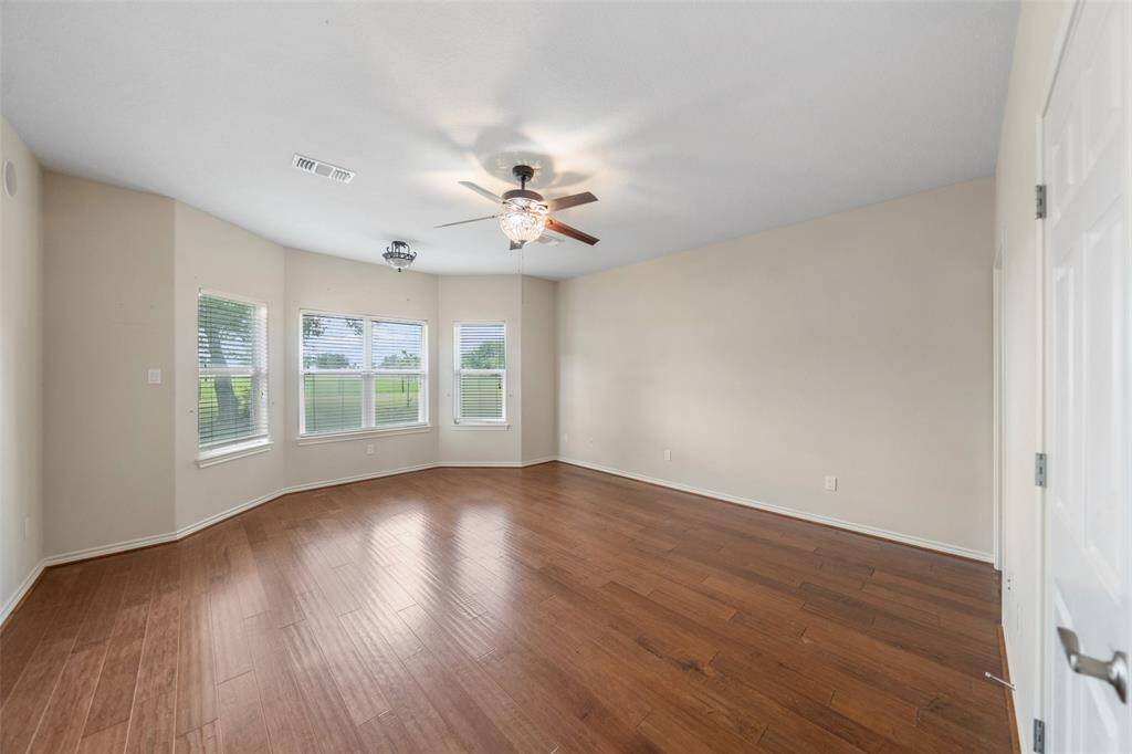 The spacious primary bedroom features a bay window that brings in natural light and views of the backyard, with wood flooring and dual ceiling fans for added comfort.