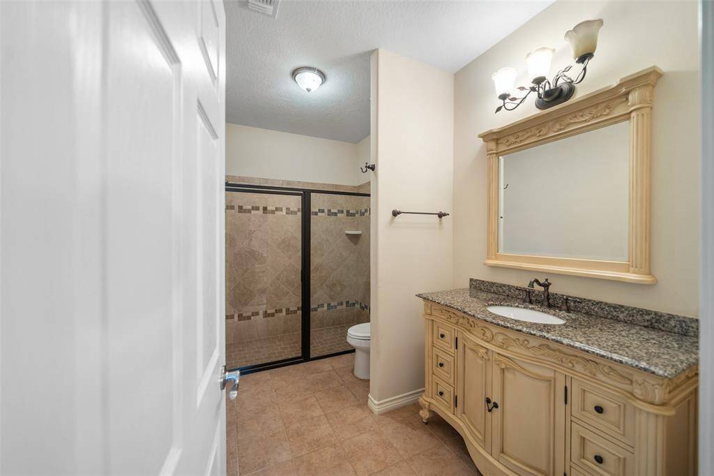 This full bath features a tiled walk-in shower, granite-topped vanity, and decorative mirror for a classic, polished look.