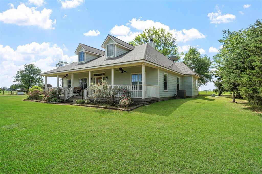 This rear view of the home highlights the spacious wraparound porch and manicured yard, creating a seamless indoor-outdoor living experience.