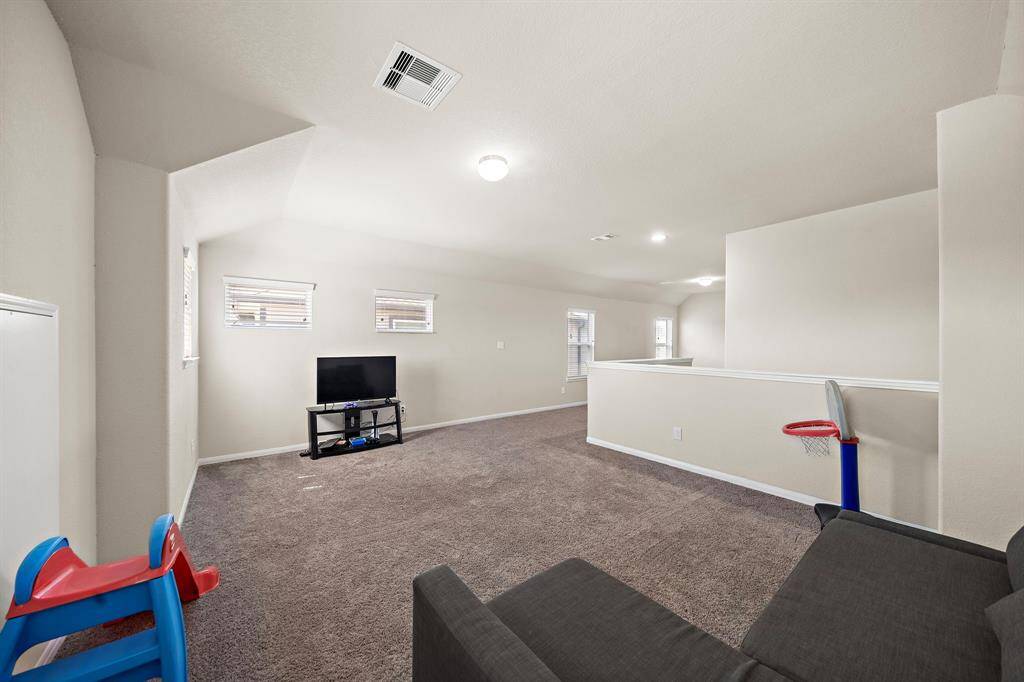 This spacious, carpeted Game room features neutral walls, recessed lighting, and multiple small windows for natural light. It includes a cozy TV area and is ideal for a family space or entertainment room.