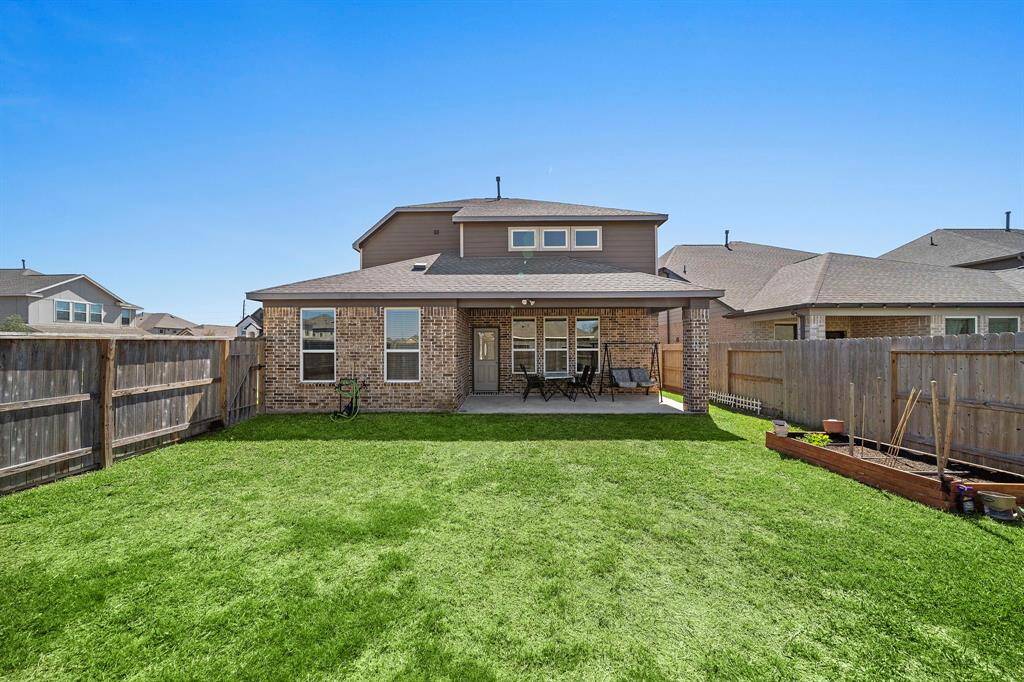 This photo shows the backyard of a two-story brick house with a covered patio, neatly fenced yard, and well-maintained lawn, ideal for outdoor activities and entertaining.