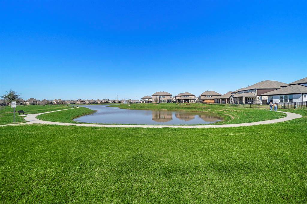 This photo showcases a serene neighborhood setting with a small pond surrounded by a walking path. The area is lined with modern houses and open green spaces, offering a peaceful suburban environment ideal for families and outdoor activities.