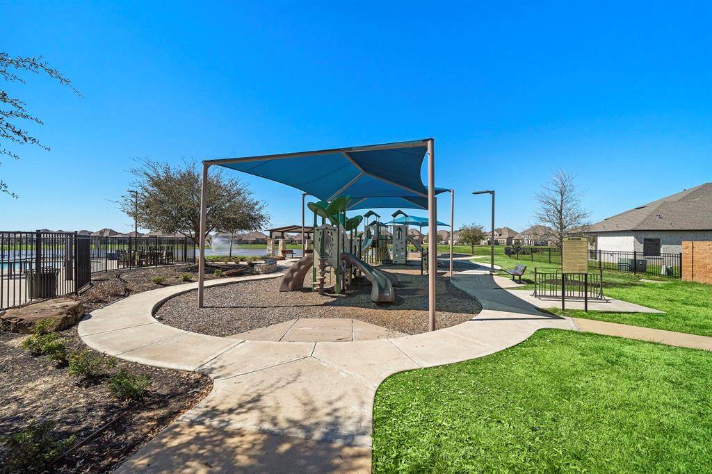 This photo showcases a community playground with slides and climbing structures, shaded by a canopy. It's surrounded by well-maintained pathways and green space, offering a family-friendly environment in a residential neighborhood.