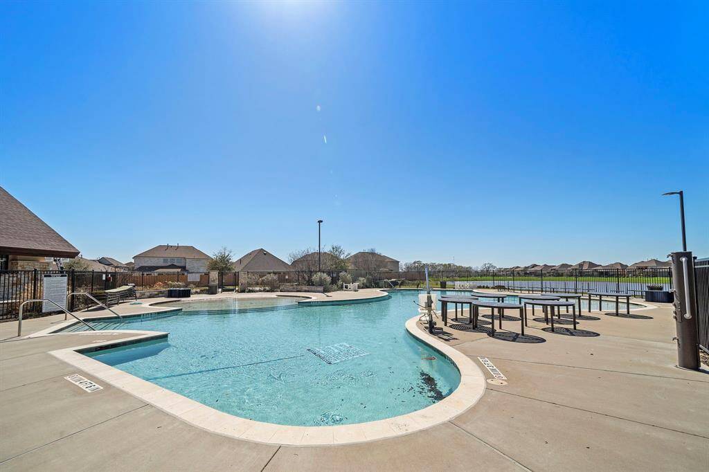 This photo showcases a well-maintained community swimming pool with a spacious deck area, perfect for relaxation and outdoor gatherings. The pool is surrounded by a secure fence and overlooks a scenic neighborhood with clear skies, enhancing the tranquil setting.