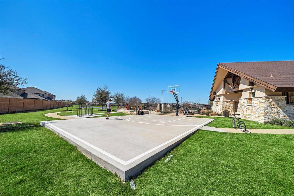 This photo showcases a community recreational area featuring a basketball court, lush green grass, and a nearby building with stone accents. Ideal for outdoor activities and sports enthusiasts.