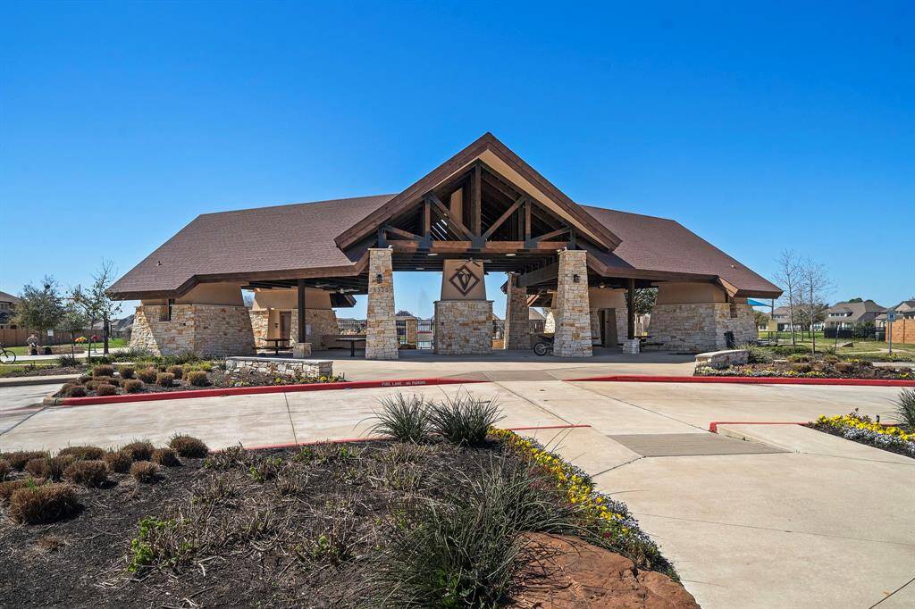 This photo features a spacious community pavilion with a rustic design, including stone pillars and a wooden roof. It's surrounded by landscaped grounds and pathways, ideal for gatherings and outdoor activities in a neighborhood setting.