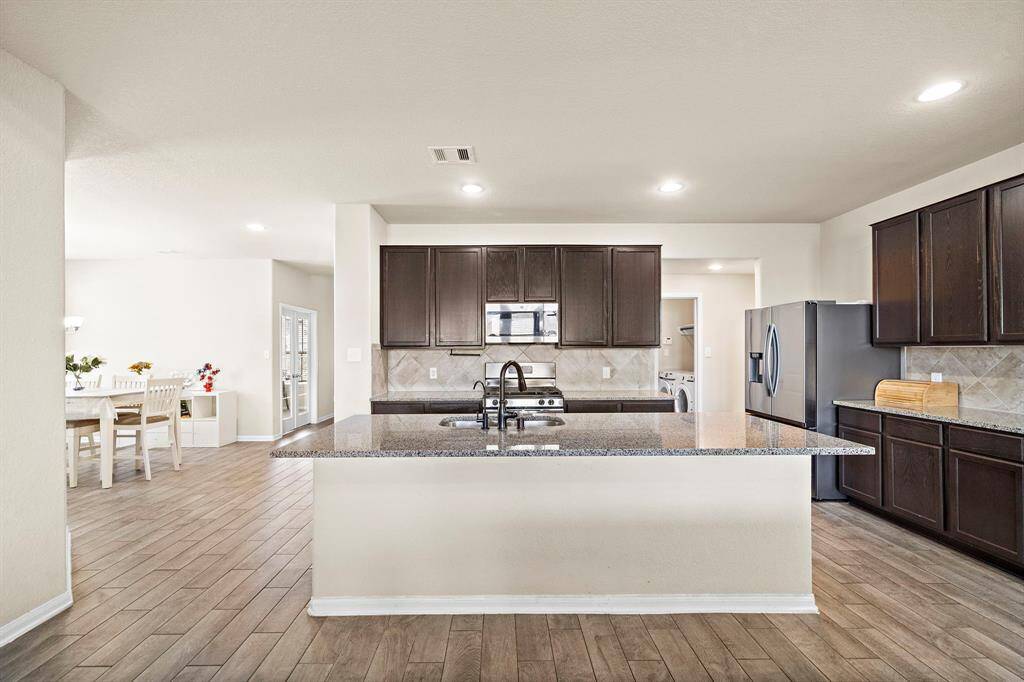 This photo showcases a spacious, modern kitchen featuring dark wood cabinetry, a large central island with a granite countertop, and stainless steel appliances. The open layout seamlessly connects to a bright dining area, creating an inviting space for entertaining.