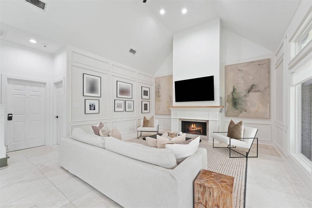 This spacious living room features a high vaulted ceiling and a modern fireplace. It has a clean, neutral color palette with large windows for natural light, a cozy seating area, and contemporary decor.