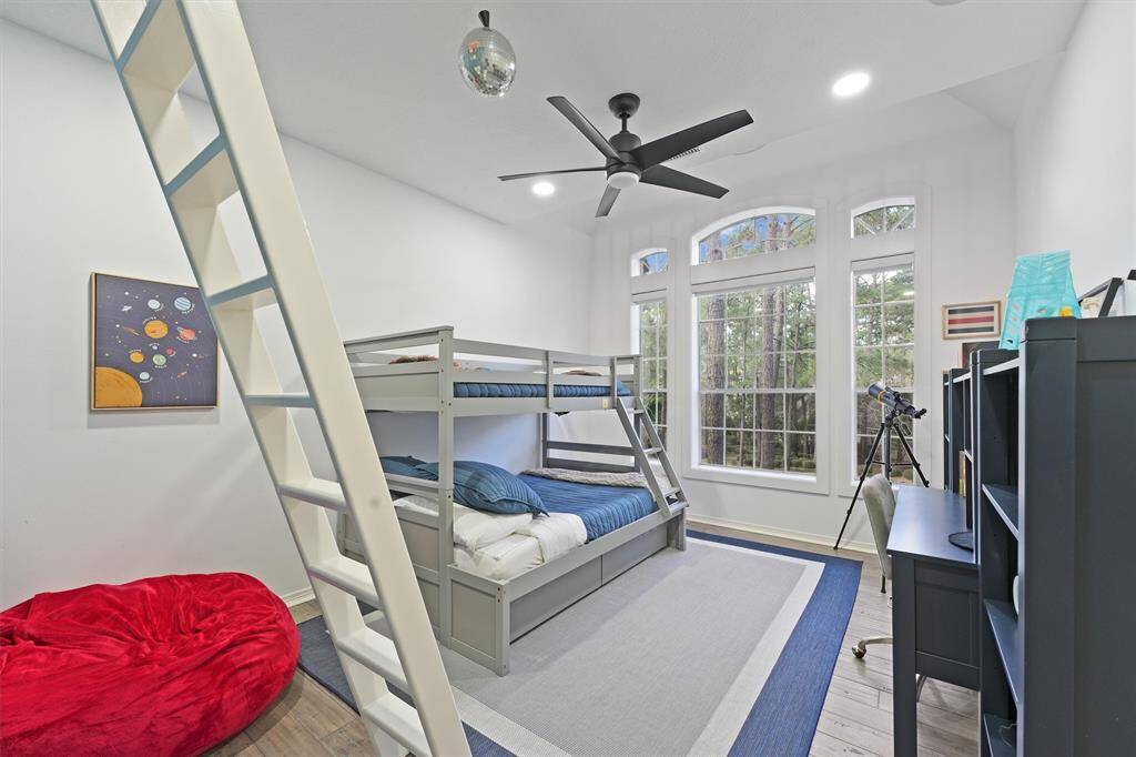 Bright and inviting bedroom with a bunk bed, large windows, and a ceiling fan. Features include a telescope, desk, and playful decor, and ladder that goes to a in-room loft perfect for a kid's space.