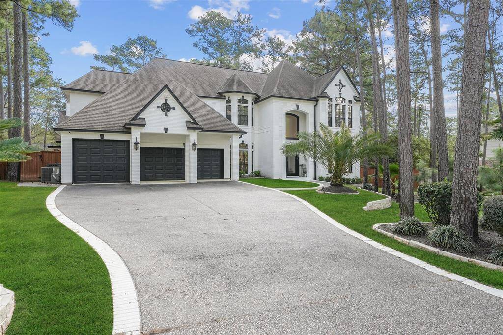 This elegant two-story home features a white brick exterior, a spacious three-car garage, and a grand entrance. Surrounded by tall trees and lush landscaping, it offers a serene, private setting with a long driveway.