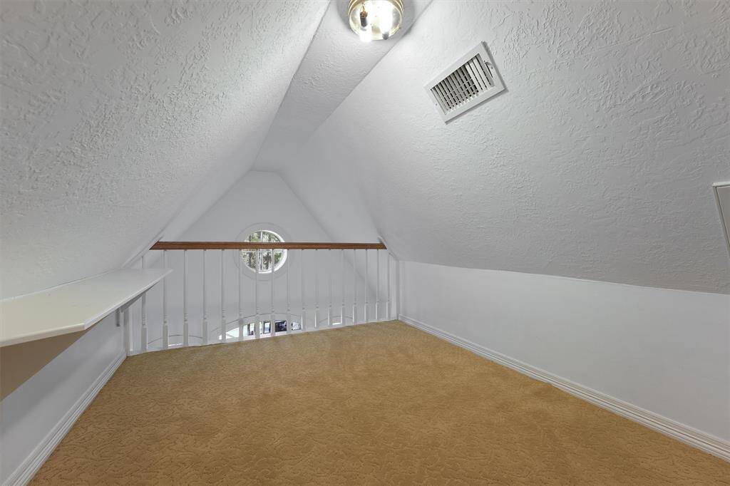 This photo shows a cozy loft space with sloped ceilings, featuring a circular window. There's a small ledge or built-in desk on one side, and a carpeted floor. Ideal for children to play and hide out