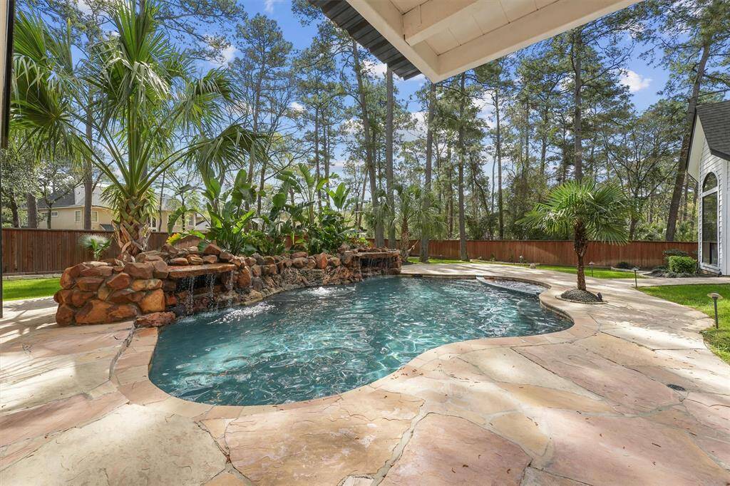 This serene backyard features a beautiful pool with a natural stone waterfall, surrounded by lush tropical landscaping and tall trees, creating a private oasis perfect for relaxation and entertainment.