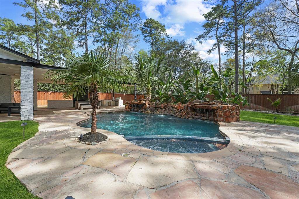 This backyard features a beautiful pool with a rock waterfall, surrounded by lush greenery and palm trees. There's a spacious patio area with seating, perfect for outdoor relaxation and entertaining.