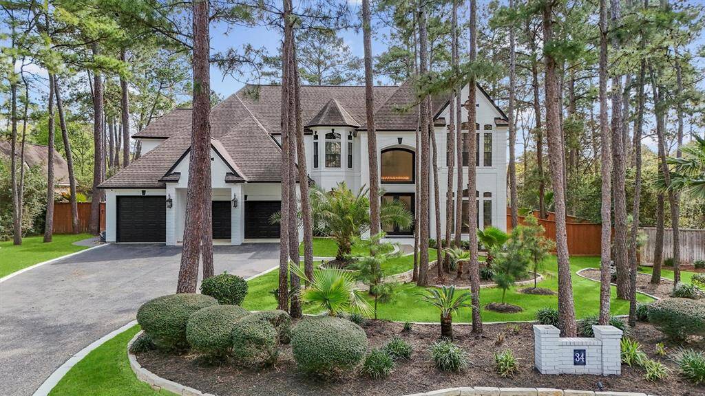 Stunning two-story home nestled among tall trees, featuring a well-manicured lawn and elegant landscaping. The house has a classic design with a gabled roof, large windows, and a three-car garage. A spacious driveway and lush greenery add to its curb appeal.
