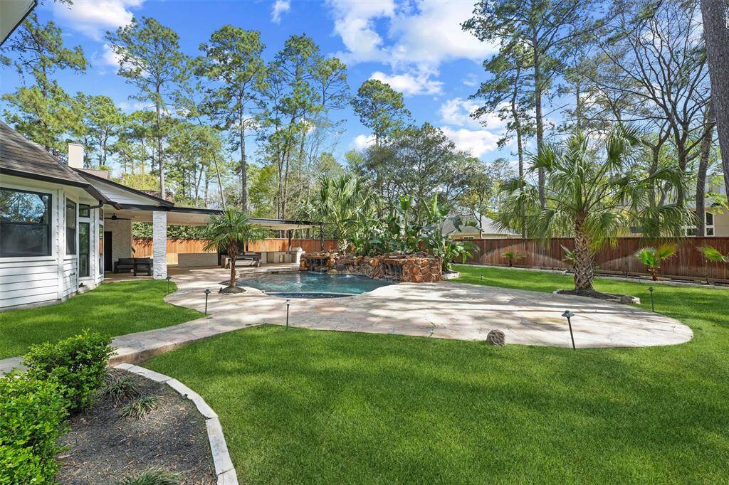 This backyard features a spacious lawn with a stone walkway leading to a pool surrounded by lush greenery and palm trees. It's perfect for outdoor relaxation and entertainment, with a covered patio area for added comfort.