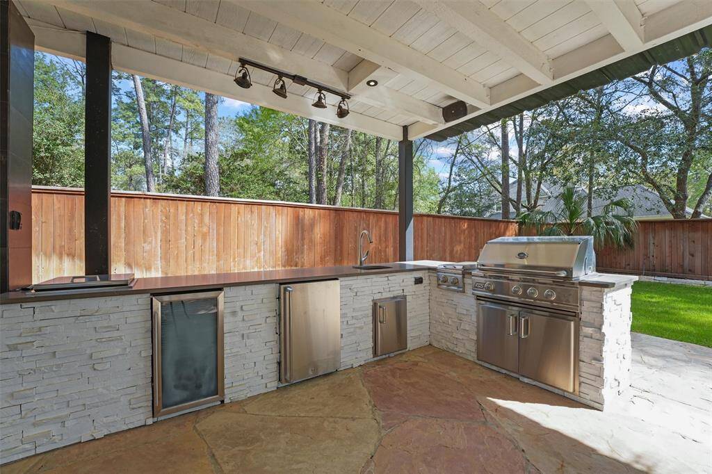 This outdoor kitchen features a covered patio with a built-in grill, mini fridge, and ample counter space. It's perfect for entertaining, with a view of the yard and surrounded by a wooden fence for privacy.