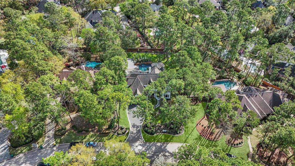 This aerial photo showcases a spacious, well-landscaped property surrounded by mature trees, providing privacy and a serene atmosphere. The home features a large yard and a pool, ideal for outdoor living, with a charming neighborhood setting.