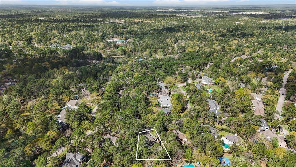 This aerial photo highlights a residential area surrounded by lush greenery, offering a serene, forested environment. The homes are nestled among trees, providing a private and tranquil setting. A specific property is outlined, indicating a potential lot for purchase.