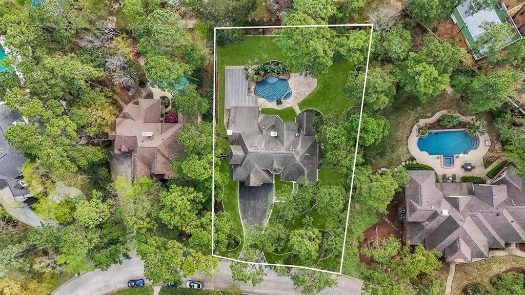 This aerial view showcases a spacious property outlined in white, nestled among lush greenery. It features a large home with multiple rooflines and a backyard pool, offering privacy and a serene environment. Perfect for those seeking a quiet, picturesque setting.